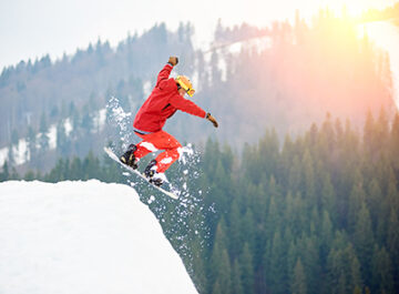 Male snowboarder freerider jumping from the top of the snowy hill with snowboard. Skiing and snowboarding concept